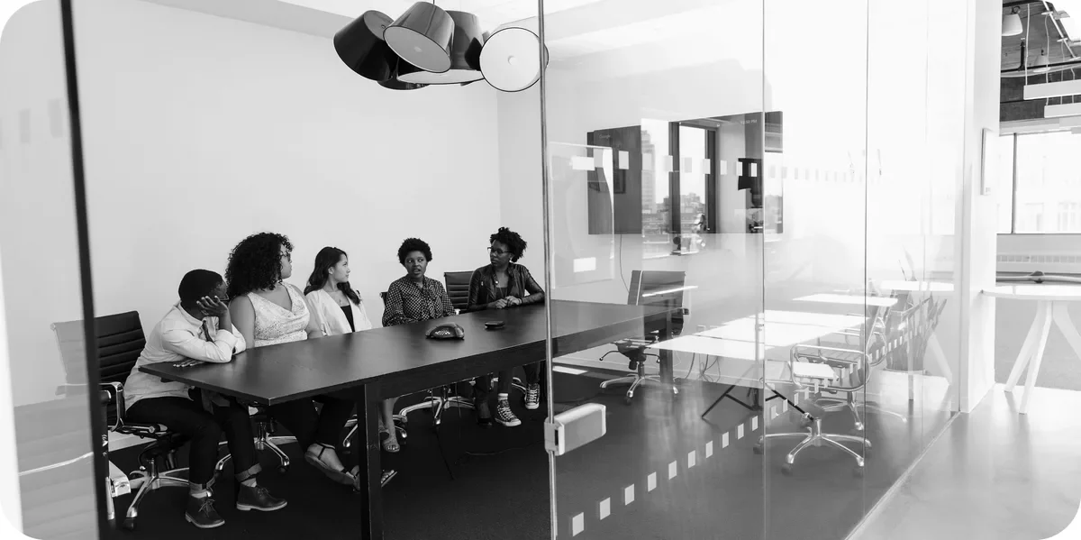 People at a long table in a glass meeting room